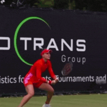 a woman in a red dress is holding a tennis racquet in front of a sign that says co rans group