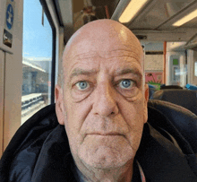 a bald man with blue eyes is sitting on a bus