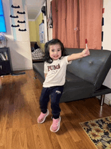 a little girl wearing a white puma shirt is holding a red lollipop