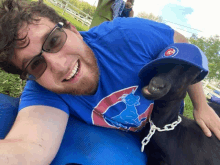 a man wearing a cubs hat is laying next to a black goat