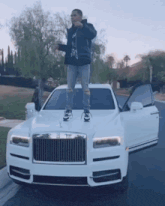 a man is standing on the hood of a white rolls royce car .