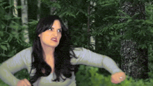 a woman with long black hair is standing in the woods making a funny face