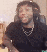 a man wearing headphones and a necklace is making a funny face while sitting in a chair .
