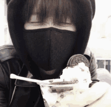 a person wearing a black mask eating ice cream with oreos