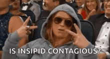 a woman wearing a hoodie and sunglasses is sitting in a crowd of people and making a funny face .