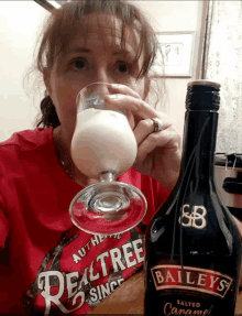 a woman drinking from a glass next to a bottle of baileys caramel