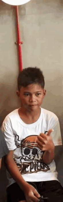 a young boy wearing a white shirt with a skull on it is sitting down .