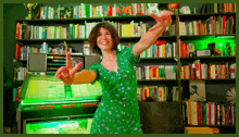 a woman in a green dress is dancing in front of a jukebox in a bookstore .