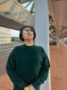 a man wearing sunglasses and a green sweater stands on a train platform