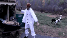 a man in a white karate uniform is standing next to a wheelbarrow with a trash can in the background that says " wet "