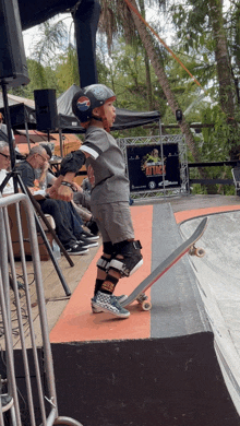 a young boy wearing a helmet and knee pads rides a skateboard down a ramp at a skateboarding event