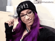 a woman with purple hair and glasses is wearing a black beanie .