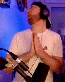 a man wearing headphones and a white shirt has his hands folded in front of a microphone