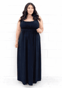 a plus size woman wearing a black dress is standing in front of a white brick wall