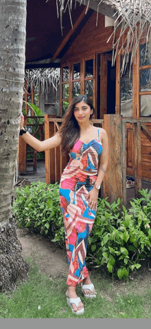 a woman in a colorful dress stands in front of a wooden hut