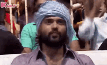 a man with a beard wearing a turban is sitting in a crowd of people .