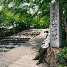 a man wearing a mask sits on a rock in front of a sign that says ' stairs ' on it