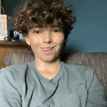 a young boy with curly hair is sitting on a couch and smiling for the camera