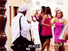 a man in a white shirt is standing in front of a group of women and says peace .