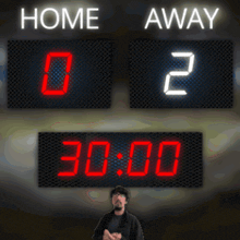 a man stands in front of a scoreboard which says home and away