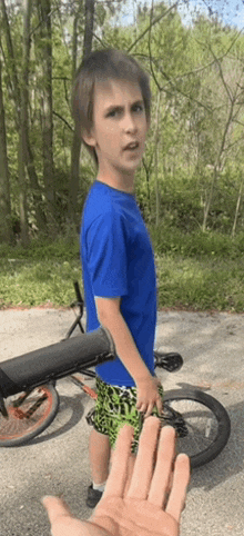 a young boy in a blue shirt is standing in front of a bicycle .