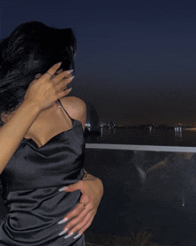 a woman in a black dress is hugging another woman in front of a body of water