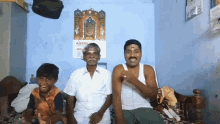 three men are sitting on a bed in front of a wall calendar that says ' odia ' on it