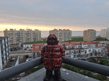 a person wearing a red and black jacket with flames on it stands on a balcony overlooking a city