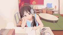 a girl wearing headphones sits at a desk writing