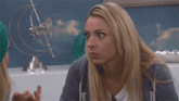 a blonde woman talking to another woman with a globe in the background