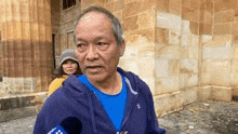 a man in a blue hoodie is standing in front of a building with a microphone .