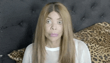 a woman is making a funny face while sitting on a bed with leopard print pillows .