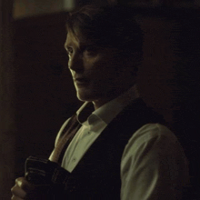 a man in a vest and bow tie is holding a wallet in his hand .