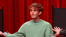 a man in a green sweater is smiling in front of a red curtain with a star academy logo