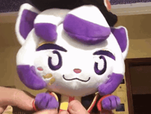 a person is holding a stuffed animal that looks like a cat with purple eyes .
