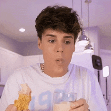 a young man drinking milk from a glass while eating a chicken wing
