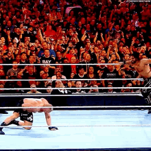 a man in a black shirt with the word bay on it is wrestling in front of a crowd .