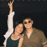 a man and a woman posing for a picture with the man wearing sunglasses and the woman wearing a green tank top