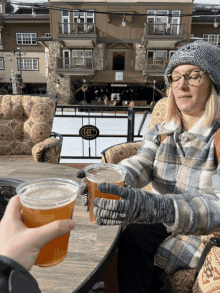 a woman sitting at a table with two cups of beer in her hands