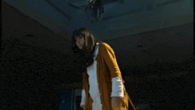 a woman in a yellow cardigan is standing in a dark room looking up at something hanging from the ceiling .
