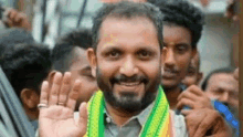 a man with a beard and a green and yellow scarf around his neck is waving at the camera .