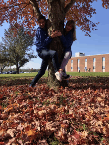 a boy and a girl hugging a tree in a field of leaves