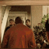 a man in a red shirt is walking through a doorway with a group of people behind him .