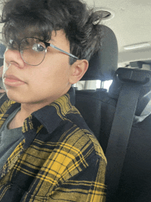 a man wearing glasses and a plaid shirt is sitting in a car