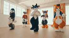 a group of furry animals are dancing in a room with one wearing a red shirt that says ' iuo '