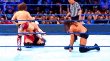 a wrestler is kneeling down in a wrestling ring while another wrestler is standing up .