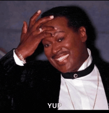 a man in a tuxedo is smiling and covering his face with his hand