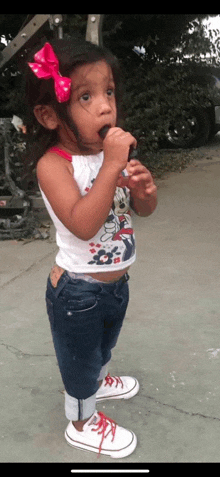 a little girl with a red bow on her head is eating a lollipop