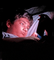 a young boy is laying in a bed looking at a cell phone .