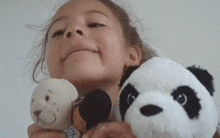 a little girl is holding three stuffed animals including a panda